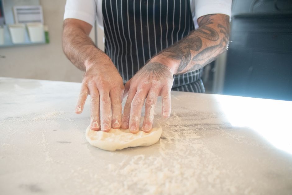 Hands actively kneading pizza dough on floured work surface