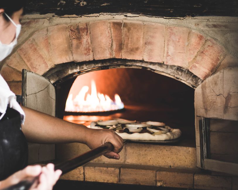 Chef expertly removing freshly baked pizza from a wood-fired oven