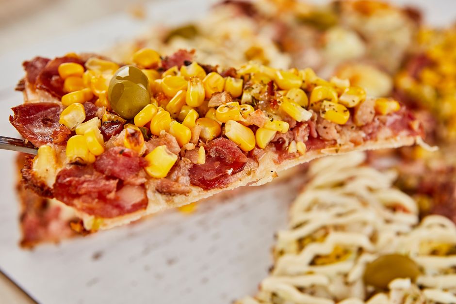 Close-up of a plated pizza slice with pepperoni, corn and olives